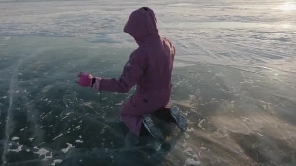 Irkutsk Region, Russia - March 18, 2021: A young girl in a pink jumpsuit slides on knees on the transparent ice of Lake Baikal. Back view. Slow motion — Stock Video