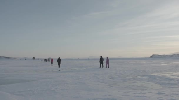 Группа туристов проходит по заснеженному льду озера Байкал к прибрежным скалам. Вид сзади — стоковое видео