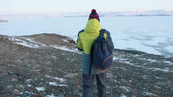 Una joven y un hombre suben la colina y admiran la hermosa vista del lago congelado Baikal en los rayos rosados de la puesta del sol — Vídeos de Stock