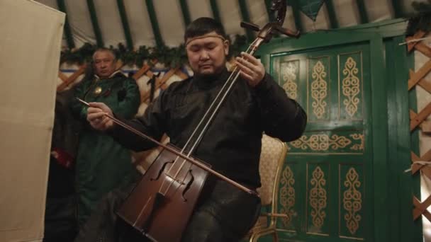 Região de Irkutsk, Rússia - 18 de março de 2021: Buryat em roupas nacionais toca um instrumento popular em uma iurta em uma excursão a um parque étnico na costa do Lago Baikal — Vídeo de Stock