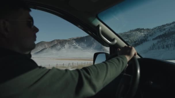 W słoneczny zimowy dzień mężczyzna prowadzi samochód i ma widok przez okno ośnieżonych gór. Zwolniony ruch — Wideo stockowe