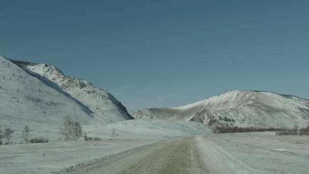 Автомобіль їде по засніженій дорозі в оточенні полів і гір. Концепція зимових подорожей. Портативний pov знімок камери — стокове відео