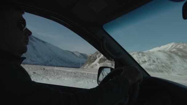 자동차의 내부에서는 운전석 뒤에 있는 남자가 창문 밖에 눈덮인 산을 바라보고 있다. 손에 들고 찍은 카메라 사진 — 비디오