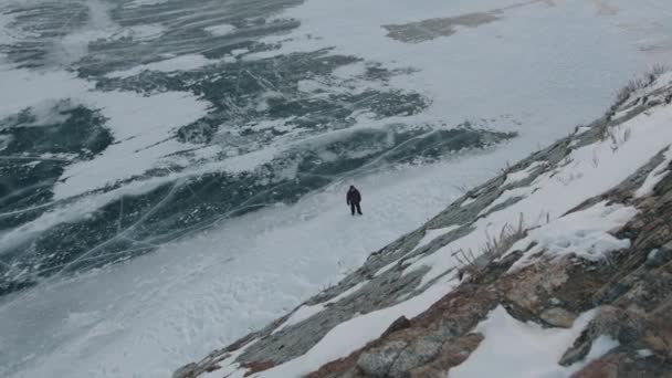 Ovanifrån av en man som står på den spruckna isen av sjön Baikal vid foten av ett berg — Stockvideo