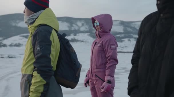 ロシアのイルクーツク地方- 2021年3月18日:観光客のグループが丘の上に立って、凍結したバイカル湖の山の海岸の背景を背景に景色を賞賛します — ストック動画
