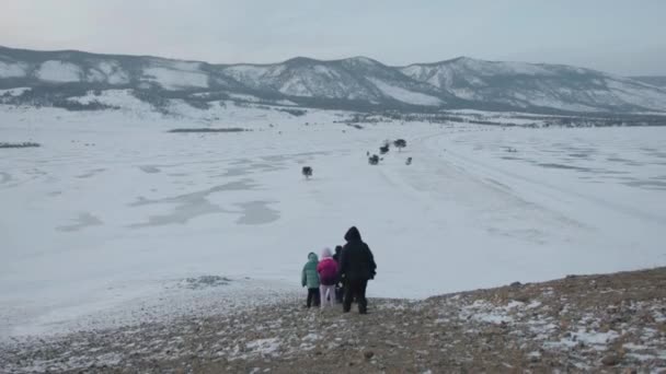 Um grupo de turistas desce a colina e vai para o Lago Baikal coberto de gelo cercado por montanhas. Visão traseira — Vídeo de Stock