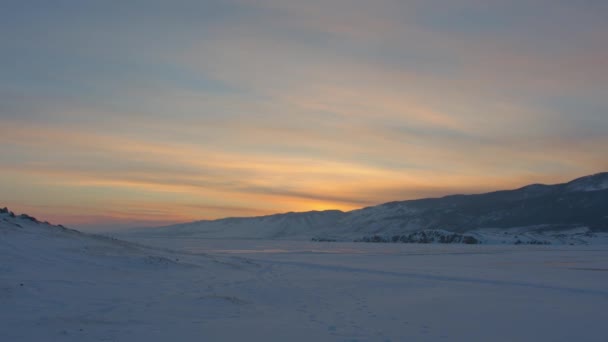 Hermoso panorama del lago congelado Baikal rodeado de montañas al atardecer y un hombre en primer plano saltando — Vídeo de stock