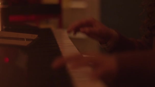 Chica joven tocando un sintetizador en una habitación semi-oscura con reflejos naranjas de velas. Primer plano. Fondo borroso — Vídeos de Stock