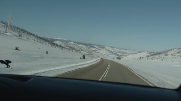 L'auto guida su una strada innevata circondata da campi e montagne. Il concetto di viaggio invernale. Colpo palmare punto di vista della fotocamera — Video Stock