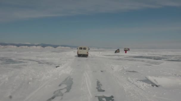 Baikal, regio Irkoetsk, Rusland - 18 maart 2021: Een konvooi van UAZ minibussen rijdt op het transparante ijs van het Baikalmeer tegen de blauwe lucht. Handheld pov shot van de camera — Stockvideo