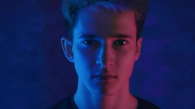 Siyah arka planda, neon ışıklı yakışıklı bir gencin portresi ve yüzünde kırmızı ışık yanıp sönüyor. 4K video