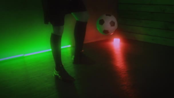 Jugador de fútbol hace malabares pelota de fútbol en un estudio oscuro con luz de neón. Concepto deportivo y estilo de vida activo. 4K — Vídeo de stock