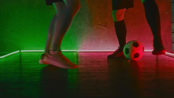 Fotbollsspelarna spelar bollen i en mörk studio med neonljus på golvet och rött och grönt ljus. 4K — Stockvideo