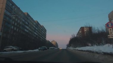 Bir kış akşamı şehir yolundaki bir arabanın ön camından ve konut binalarından bakın. Kameranın el kameralı görüntüsü 