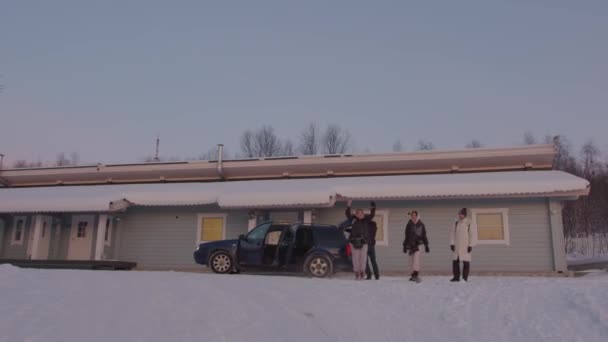 Мурманськ, Росія - 10 січня 2021 року: дівчата танцюють і дуріють, стоячи в снігу біля автомобіля і готельного будинку. Веселі зимові подорожі. — стокове відео
