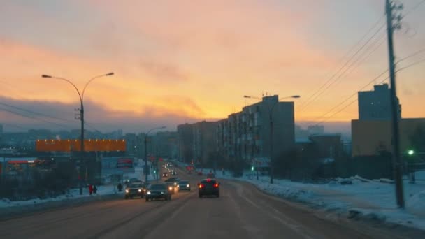 Murmansk, Rusland - 10 januari 2021: Druk verkeer op de weg van de winterstad en uitzicht op de huizen bij zonsondergang — Stockvideo