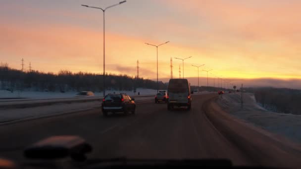 러시아, 무르만스크 - 2021 년 1 월 10 일: 교외 고속 도로에서 노을을 배경으로 한 송전선 과 송전선 이 많은 차량. 겨울 여행의 개념 — 비디오