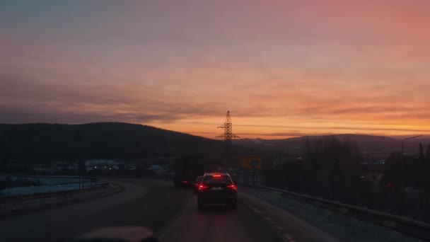 Murmansk, Russia - 10 січня 2021: Ряди автомобілів на приміському шосе в сутінках і вид снігових пагорбів і веж передачі електроенергії на заході сонця. — стокове відео