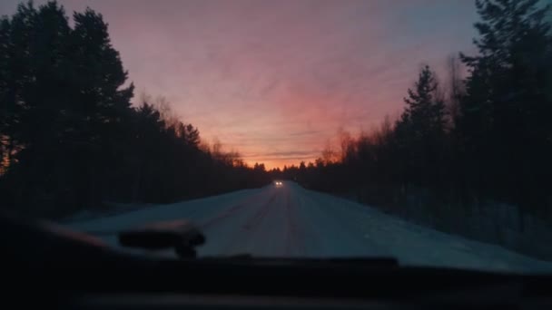 Vista della foresta innevata sullo sfondo di un cielo arancione attraverso il parabrezza dell'auto. Colpo palmare punto di vista della fotocamera — Video Stock