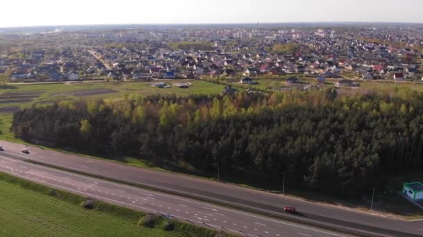 Drone tiro di una pista con auto circondate da boschi e prati e una grande città con cortili privati alla periferia — Video Stock