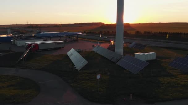 Minsk, Vitryssland - 20 maj 2021: Drönare skytte rader av solpaneler och väderkvarn nära en bensinstation och en förort väg vid solnedgången — Stockvideo