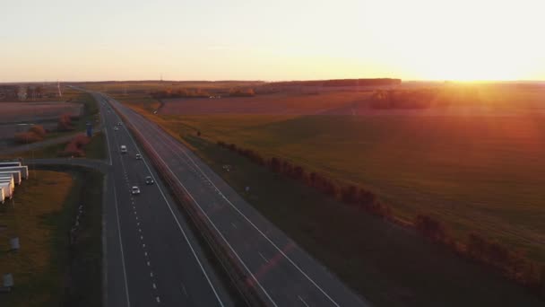 Vista aérea de uma movimentada rodovia suburbana e bela paisagem rural com campos verdes e floresta ao pôr do sol — Vídeo de Stock
