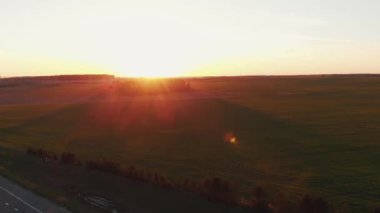 Gün batımında orman ve çayırlarla dolu güzel bir yaz manzarasının insansız hava aracı çekimi ve taşra yolunda yoğun bir trafik