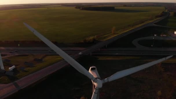 Drohne schießt Nahaufnahme der Rotorblätter einer Windmühle vor dem Hintergrund grüner Wiesen und einer viel befahrenen Vorstadtautobahn — Stockvideo