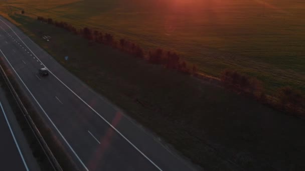 Widok z powietrza na ruchliwą podmiejską autostradę i piękny krajobraz wiejski z zielonymi polami i lasem o zachodzie słońca — Wideo stockowe