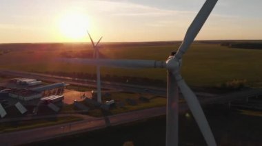 Bir yel değirmeninin dönen bıçaklarını çevreci çayırların ve işlek bir banliyö otobanının arka planına yakın çekim yapan drone.