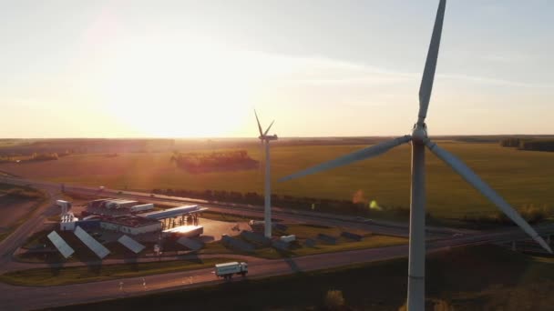 Drone photographiant en gros plan les pales tournantes d'un moulin à vent sur fond de prairies verdoyantes et d'une autoroute de banlieue animée — Video