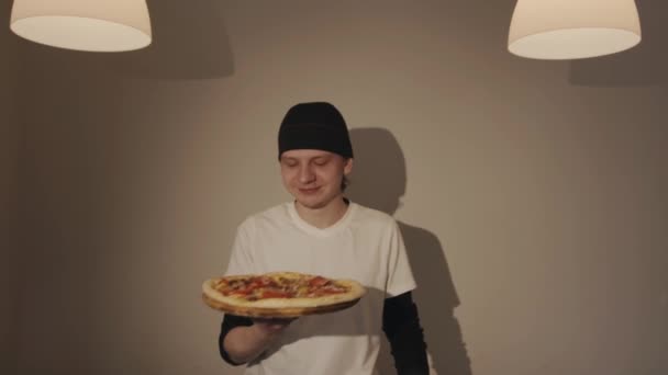 Un joven chef en un pañuelo sostiene una pizza en un café y la huele disfrutando del aroma — Vídeo de stock