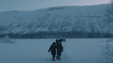 Bir grup turist kış ormanı ve dağların zemininde karla kaplı bir patika boyunca yürüyor. Arka plan