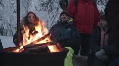 Murmansk, Rusya - 10 Ocak 2021: Gençler yürüyüş sırasında ateşin başında oturup konuşuyorlar. Arkadaşlık ve birliktelik kavramı