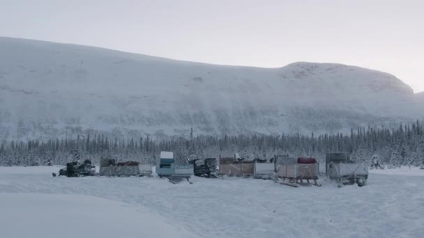 Estacionamento em uma estrada nevada de motos de neve com um trenó de madeira ligado a eles para o transporte de turistas — Vídeo de Stock