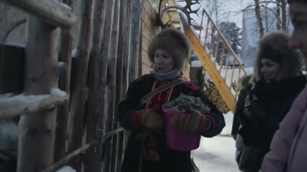 Murmansk, Russia - 10 gennaio 2021: Una donna in abiti etnici e un gruppo di giovani ragazze sono in piedi su una strada innevata del villaggio e parlano — Video Stock