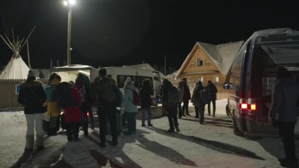 Murmansk, Rusia - 10 de enero de 2021: Un grupo de turistas durante un viaje de invierno llegó por la noche en minibuses y se encuentra en la calle cerca del complejo hotelero del pueblo — Vídeos de Stock