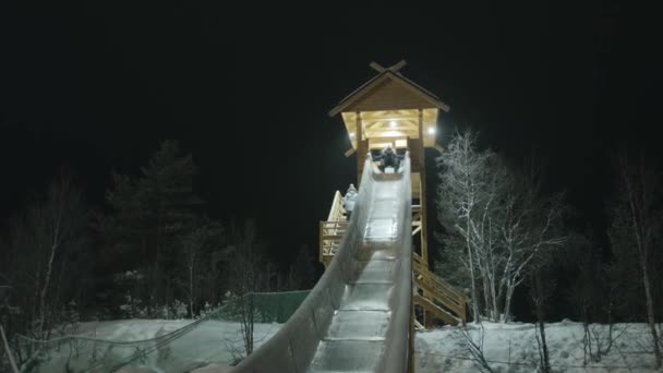 Mladý muž jezdí na zadním sedadle na velkém dřevěném skluzavce na venkovském panství za zimního večera — Stock video