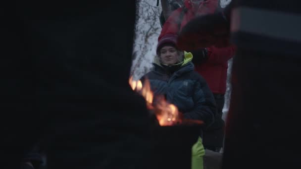 Murmansk, Rusland - 10 januari 2021: Jongeren zitten tijdens de wandeling bij het vuur in het winterbos en praten. Vriendschap en saamhorigheid — Stockvideo