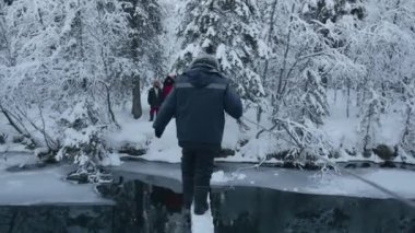 Bir adam, bir kış ormanında ahşap bir köprünün üzerinden nehri geçiyor ve bir ipe tutunuyor. Arka plan