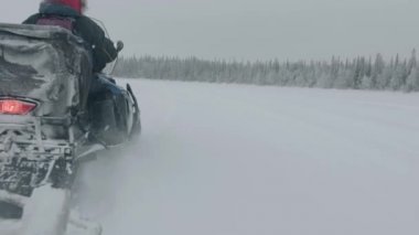 Murmansk bölgesi, Rusya - 10 Ocak 2021: Turistler kar tarlasında kar motosikletine biniyorlar. Arkadan bak. Kameranın el kameralı görüntüsü
