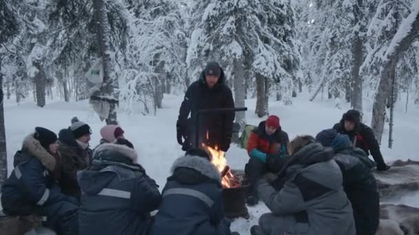Мурманська область (Росія) 10 січня 2021 року: група туристів сидить довкола багаття в зимовому лісі й розповідають одне одному історії. — стокове відео