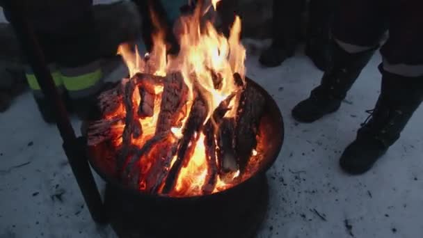 Een groep toeristen staat rond een ijzeren haard met een kampvuur. Winterreizen — Stockvideo