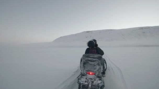 I turisti cavalcano una motoslitta attraverso un campo innevato verso la montagna. Vista posteriore — Video Stock