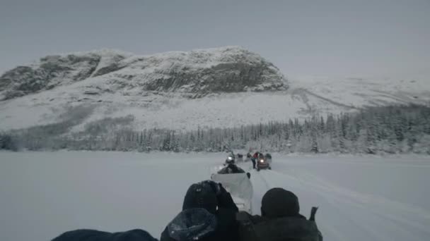 Murmansk region, Russia - January 10, 2021: Snowmobiles carry tourists in sleighs at polar night. Back view. Handheld pov shot of camera — Vídeos de Stock