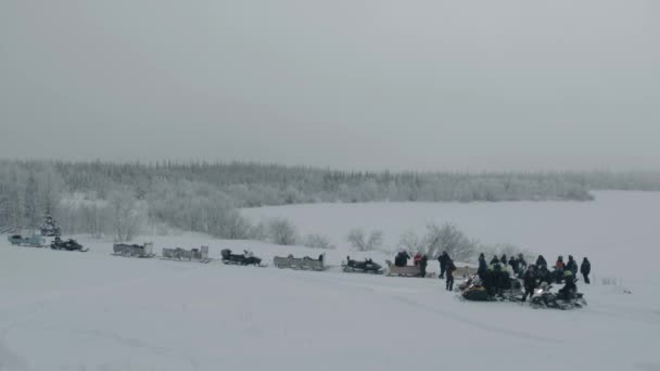 Parking of snowmobiles with sledges and a group of tourists near the winter forest — стоковое видео