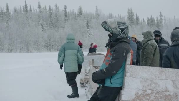 Murmansk region, Russia - January 10, 2021: Snowmobile driver in a helmet and a group of tourists stand near a sled for trips to nature — стоковое видео