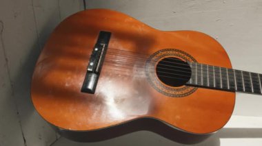 Klasik bir akustik gitar desenli beyaz duvarları ve zemini olan bir odanın köşesinde durur. Dikey video