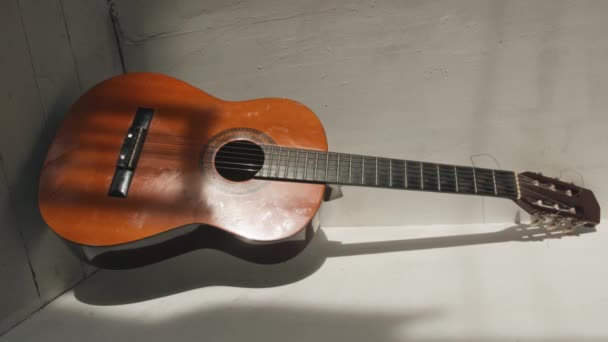 A classical guitar stands in the corner of the room against the backdrop of textured white walls. Vertical video — Vídeos de Stock