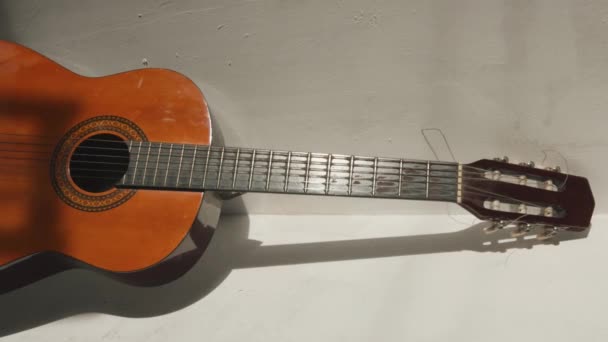 Klasická akustická kytara sedí v rohu místnosti s texturovanými bílými stěnami a podlahou. Svislé video — Stock video